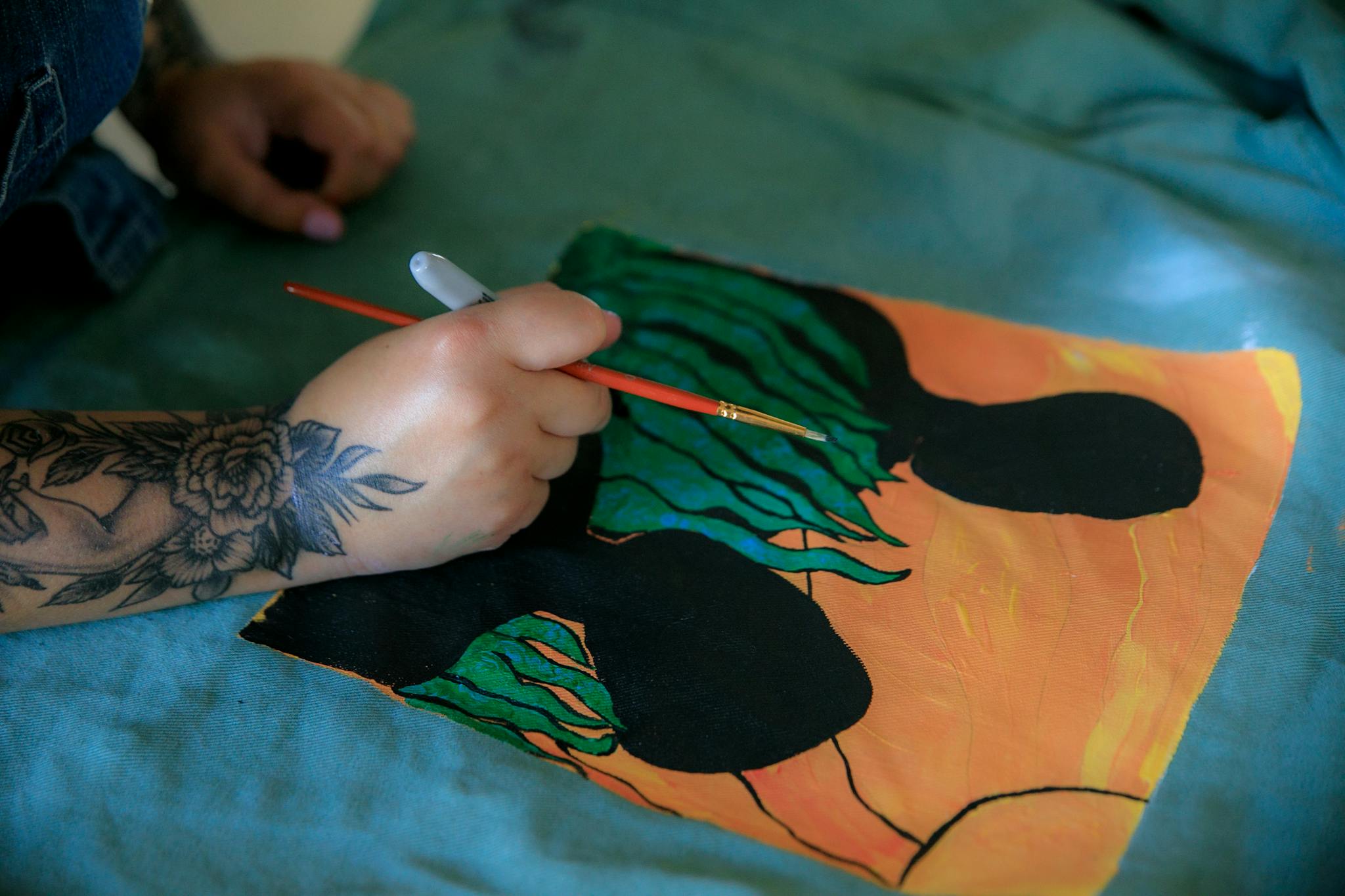 Close-up of artist painting a colorful design on fabric with a brush. Emphasizes creativity and craft.