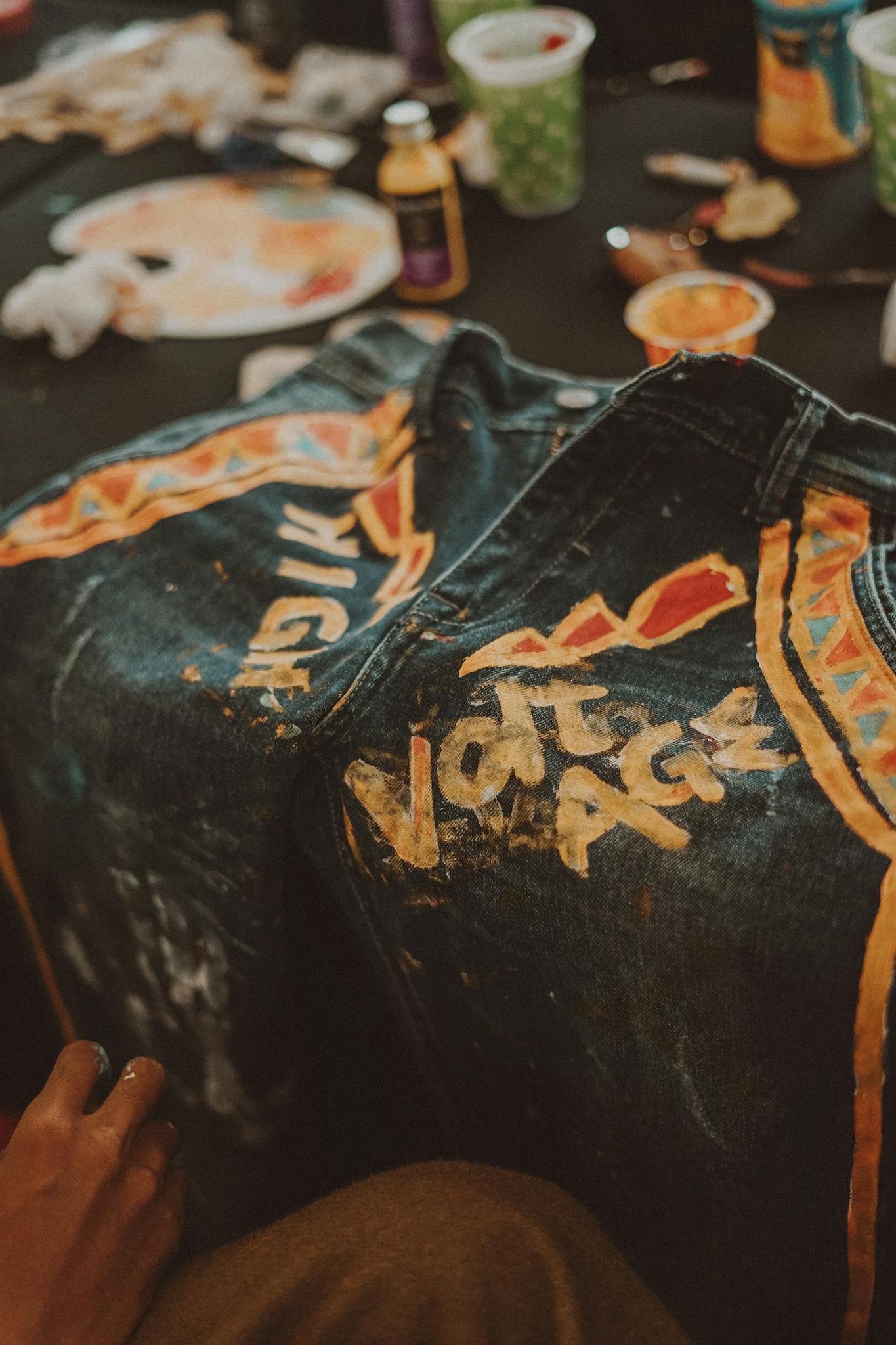 Close-up of hand-painted blue jeans featuring vibrant patterns and text against a background of art supplies.