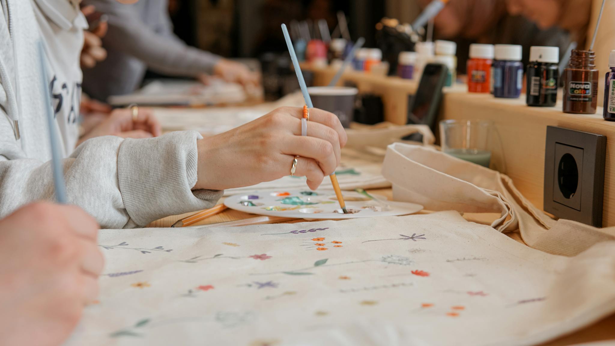 Close-up of hands painting floral designs on fabric using a palette in an art studio.
