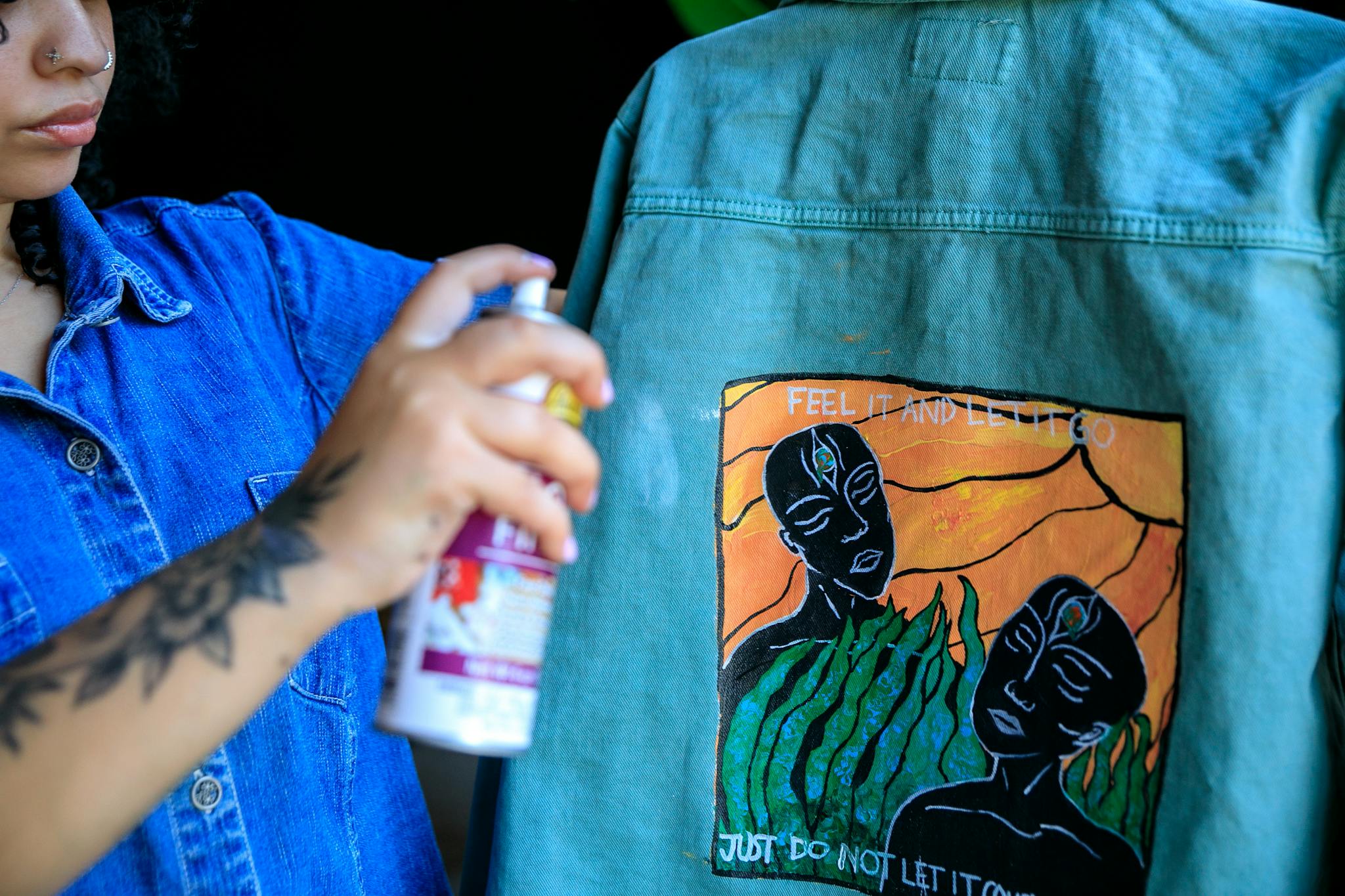 Woman artist spray painting a denim jacket with unique artwork design.